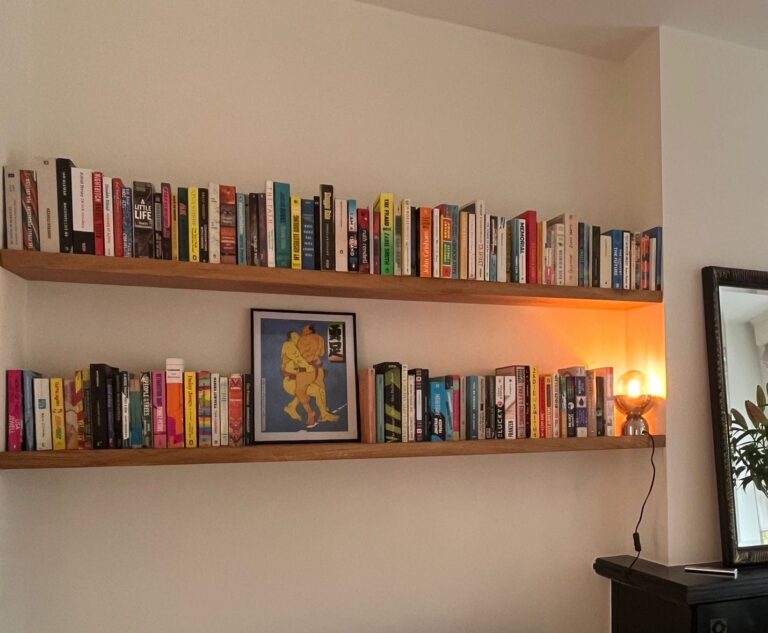 Twee eiken boekenplanken naast een schouw en een grote spiegel