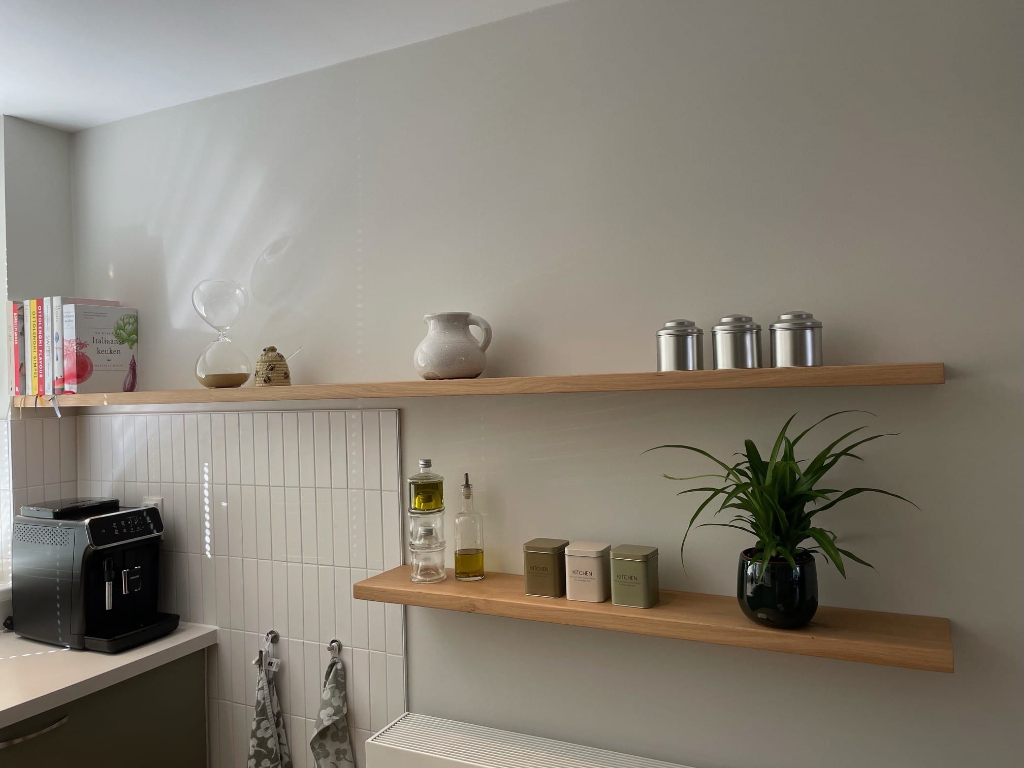 Twee zwevende eiken wandplanken met voorraadbussen en een plant in een lichte keuken