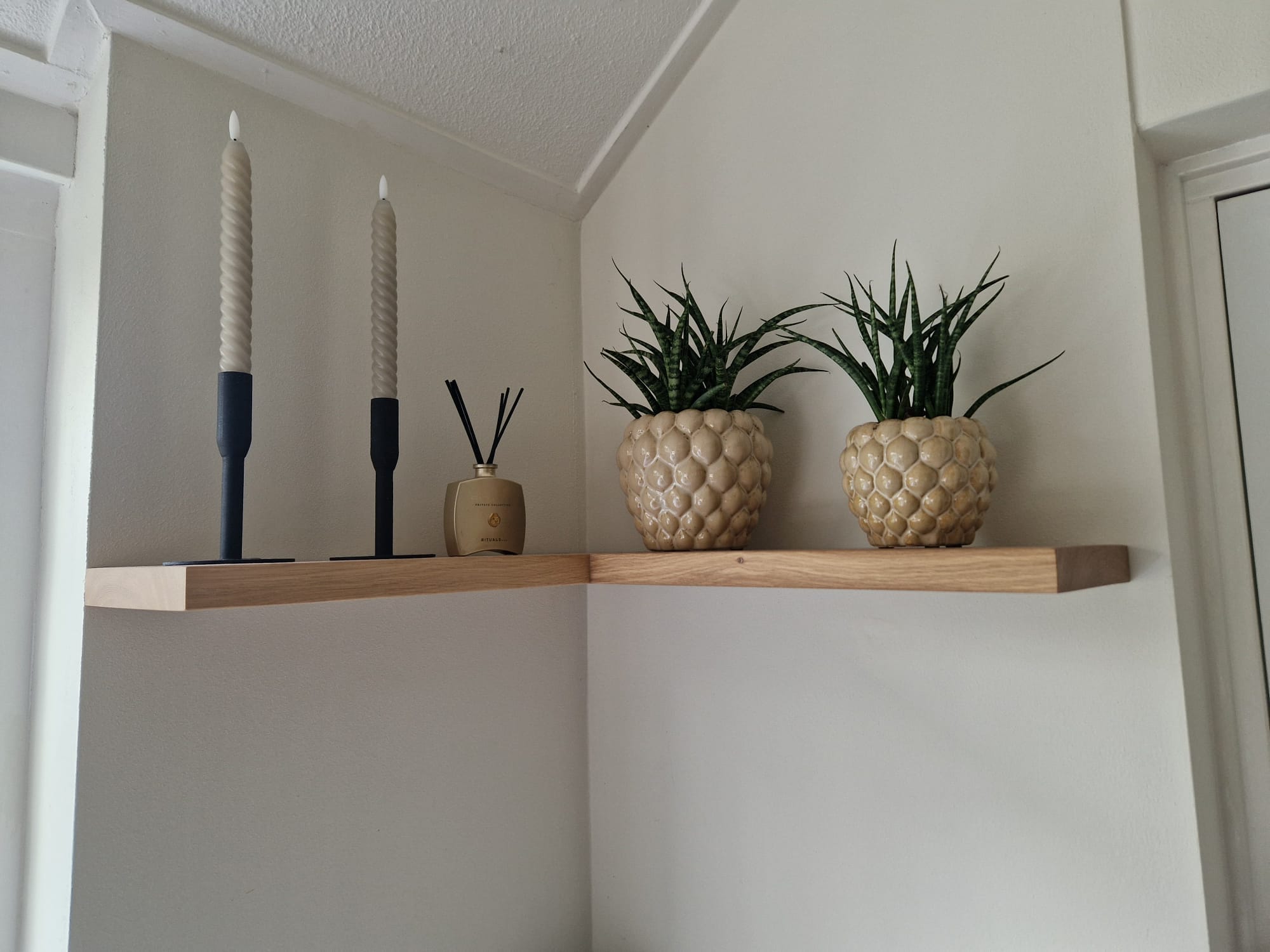 Eiken hoekplank met planten en kandelaars tegen witte muren