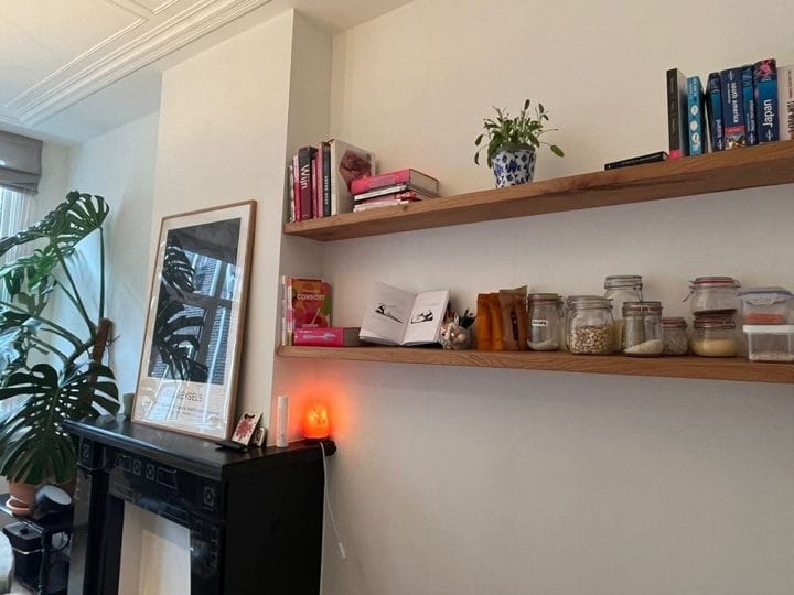 Twee eiken wandplanken met boeken en decoratie naast een schouw, spiegel en grote plant