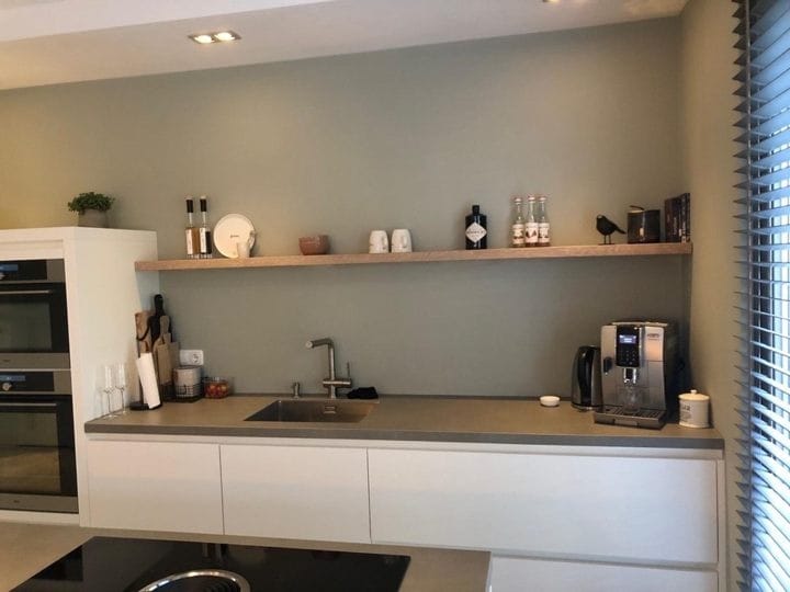 Lange zwevende eiken wandplank boven het aanrecht in een lichte keuken