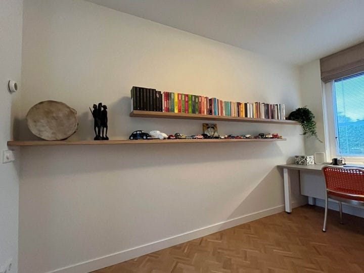 Twee zwevende eiken wandplanken met boeken en decoratie boven een houten vloer