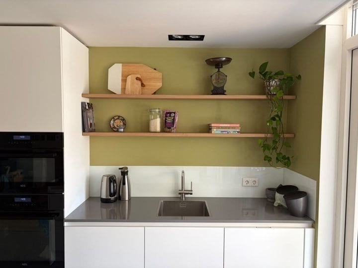 Twee rechte zwevende eiken wandplanken tegen een groene keukenwand