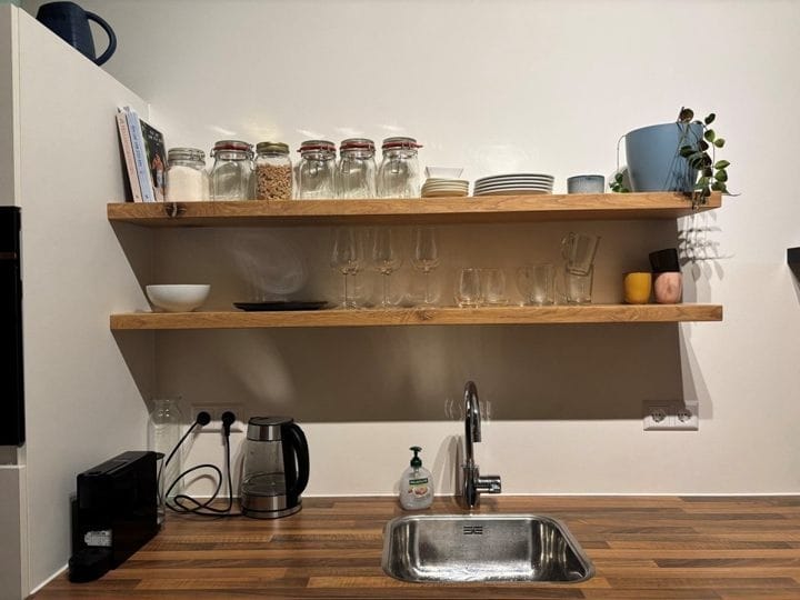 Twee zwevende eiken wandplanken met voorraadpotten, servies en glazen boven de spoelbak